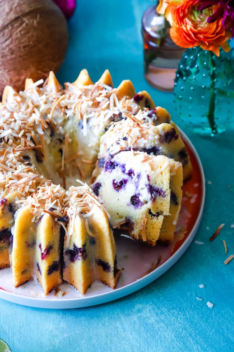 Bundt cake on red plate sliced to show the interior of the cake studded with blueberries. 