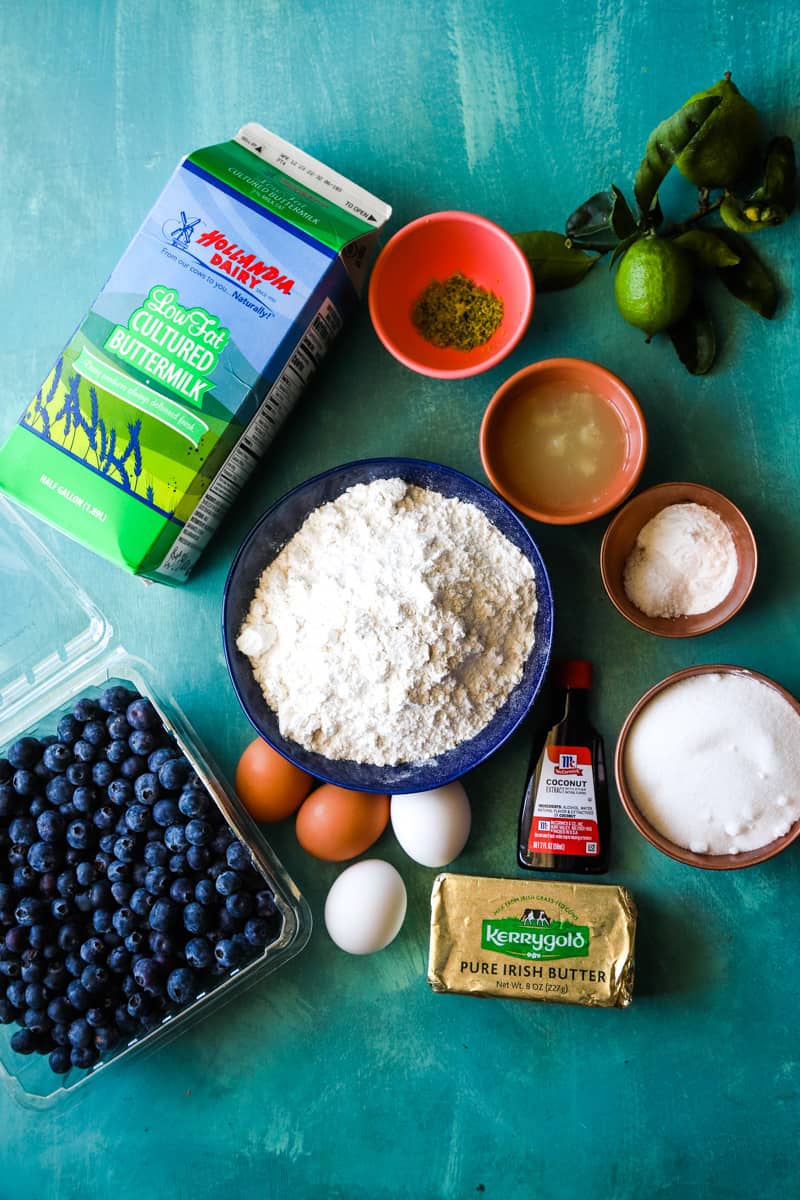 Ingredients to make the lime coconut blueberry bundt cake in small bowls on a teal background. 