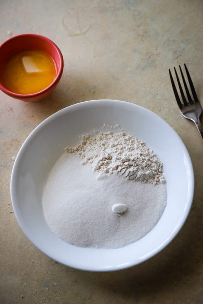 Flour and sugar in a large white bowl with small bowl of melted butter. 