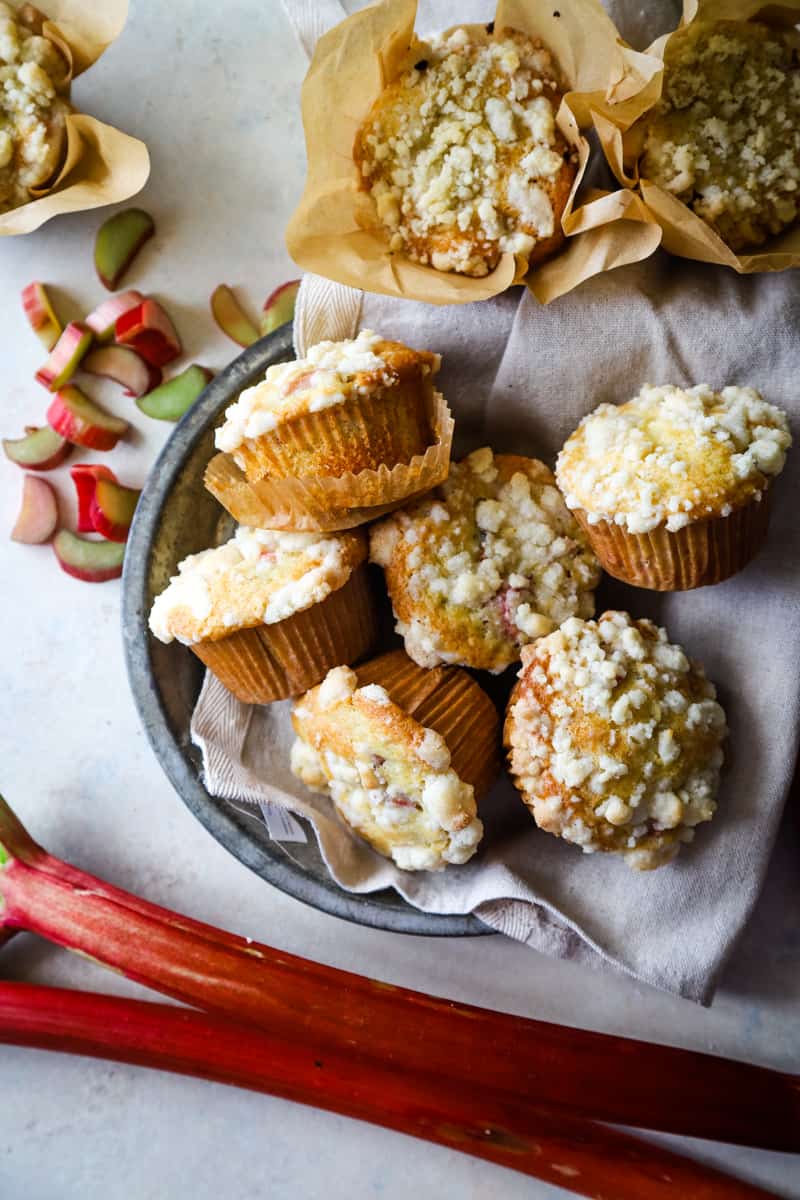 Bakery style muffins piled in a round dish lined with beige dishtowel. 