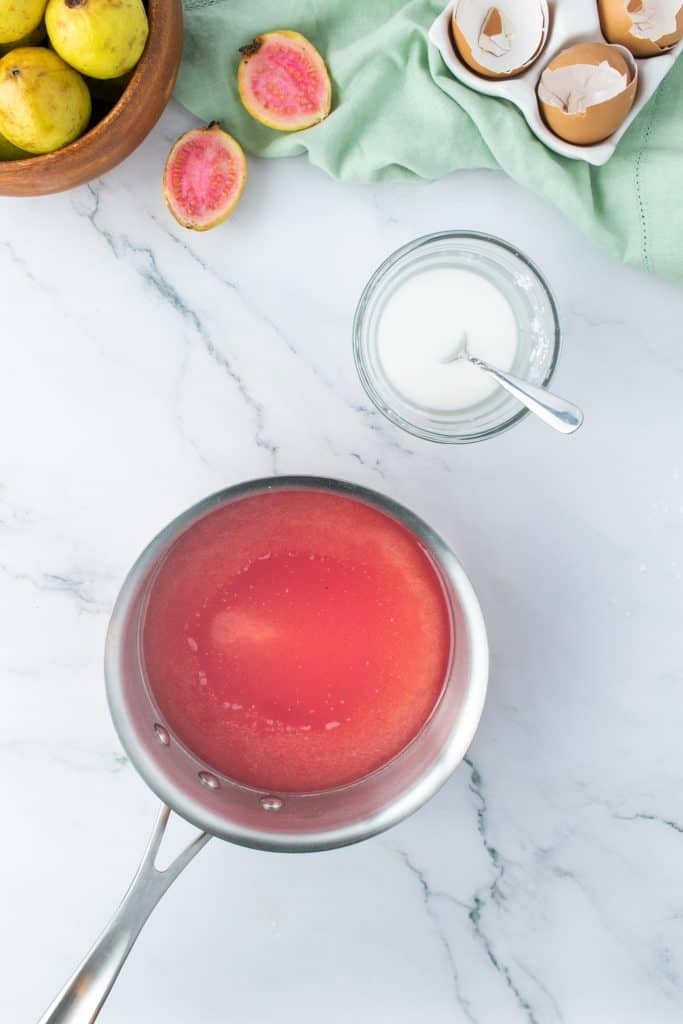 Guava juice in a metal saucepan on white marble background. 