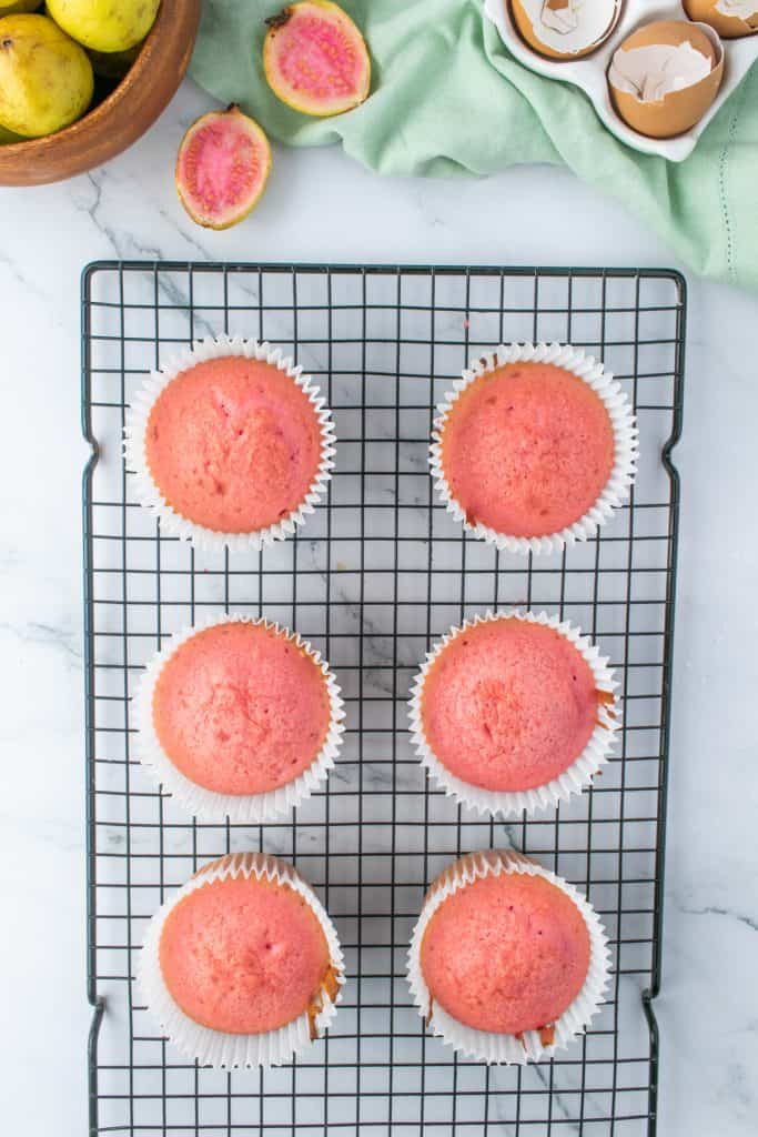 Overhead shot of pink cupcakes on a wire cooling rack on marble background. 