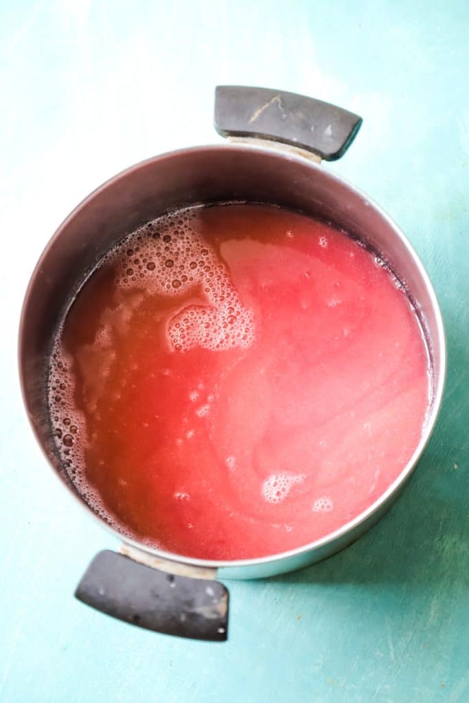 Large Sauce pan with pink rhubarb syrup on teal background. 