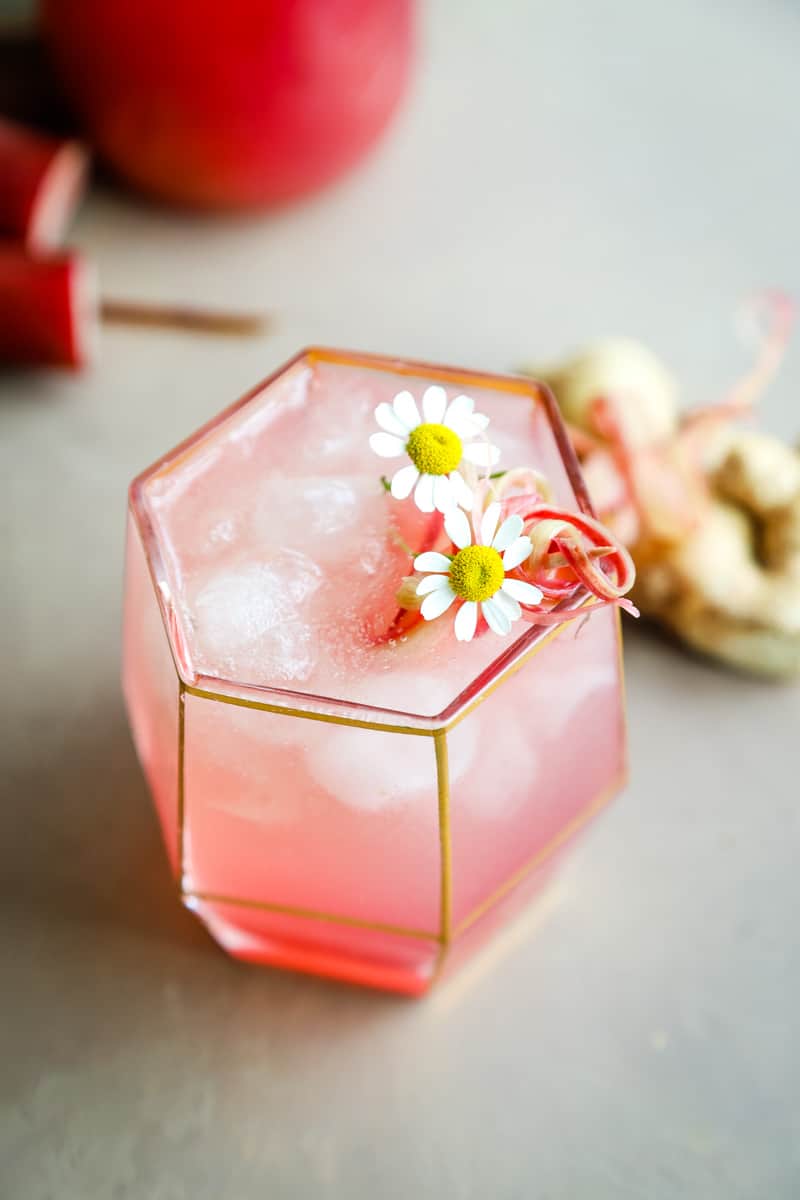 Top of the pink rhubarb cocktail garnished with chamomile flowers and shaved rhubarb. 