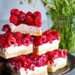 Stacked raspberry cream cheese bars in metal plate with flowers in background.