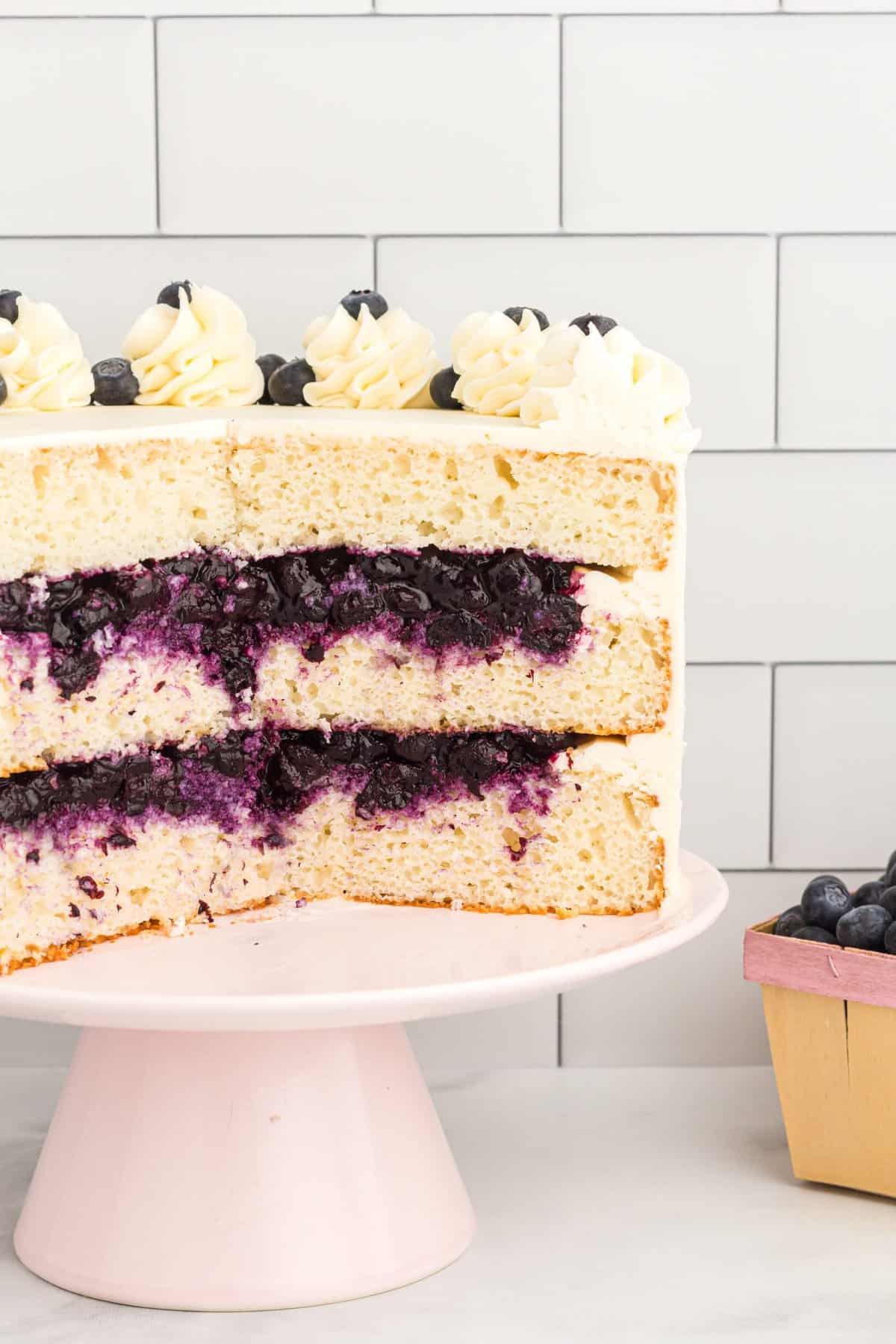 Whole cake on pink stand with slices removed to show the blueberry filling. 