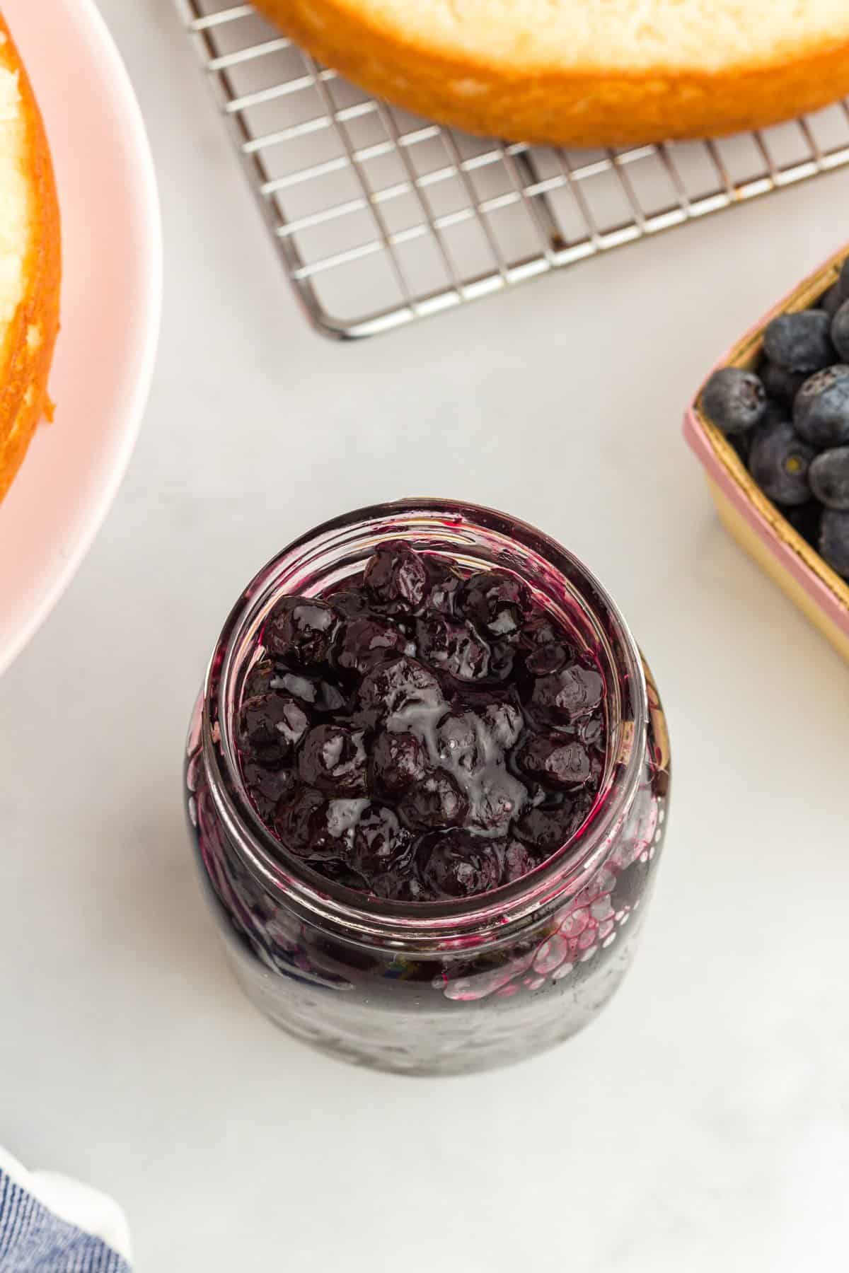 Blueberry cake filling in a small mason jar with cake layers in background. 