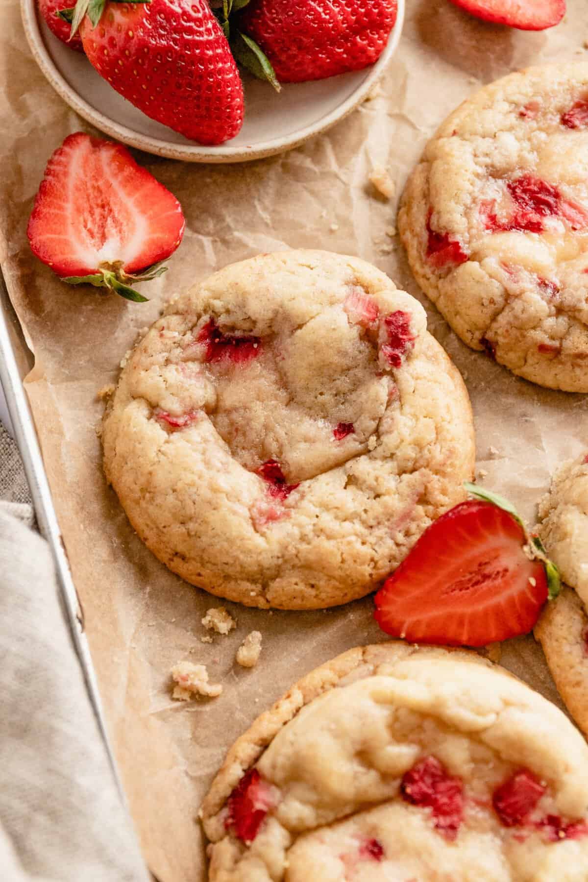Cookies on brown paper next to a bowl of fresh strawberries on a tray. 