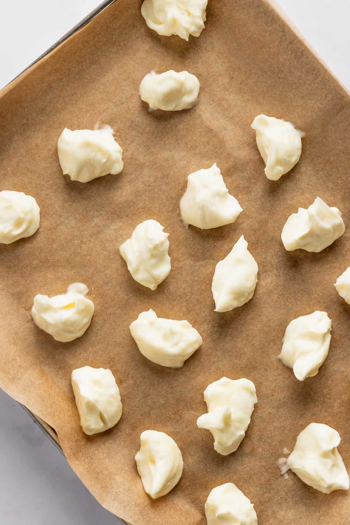Balls of the cheesecake mixture on a parchment lined baking sheet. 