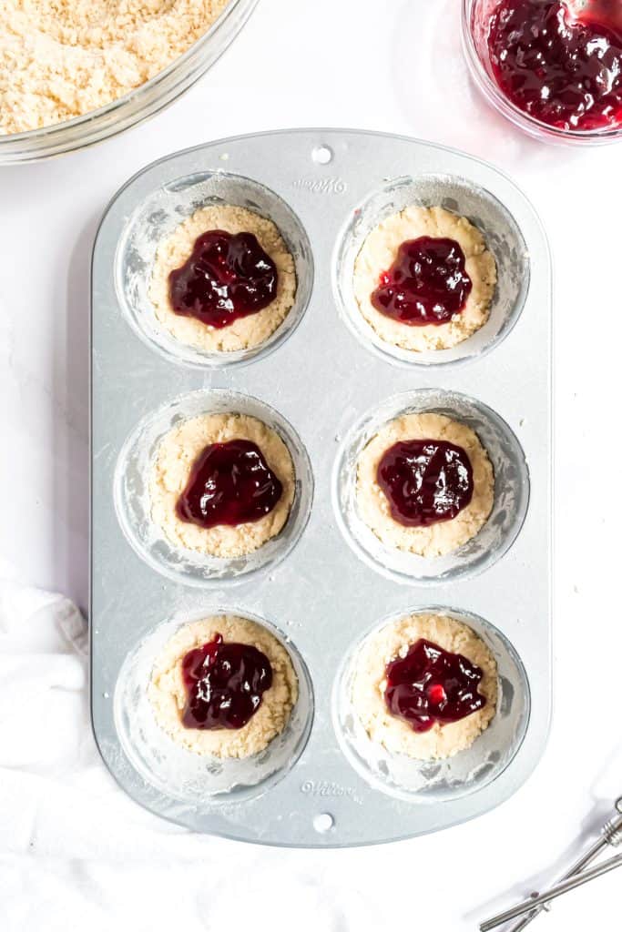 Adding the raspberry filling to the center of each muffin tin over crust. 