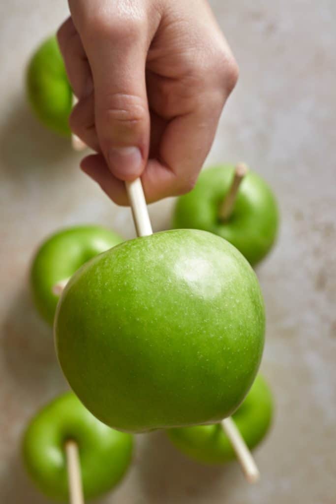 Hand sticking stick into green apple to make caramel apples. 