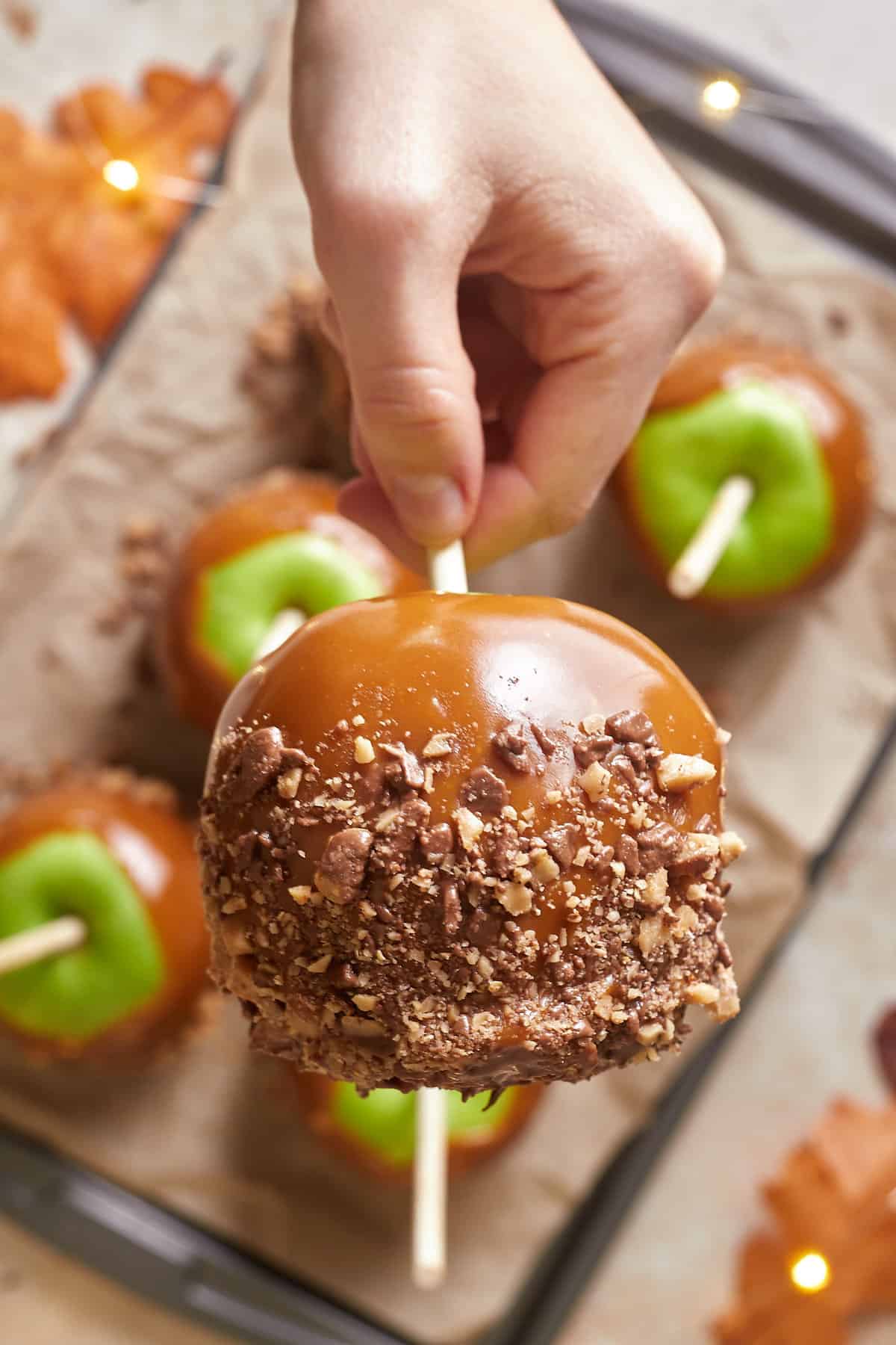 Hand holding a green caramel apple that has been coated in toffee pieces. 