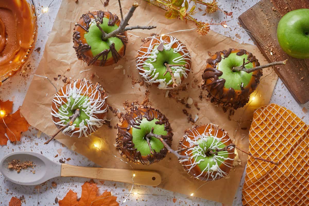 Overhead shot of six green caramel apples on a sheet of brown parchment paper. 