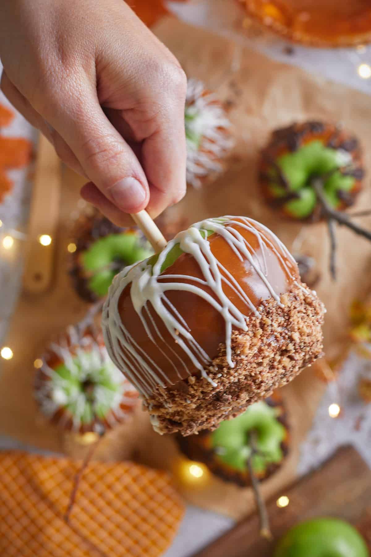 Hand holding a caramel apple with toffee bits and white drizzle. 