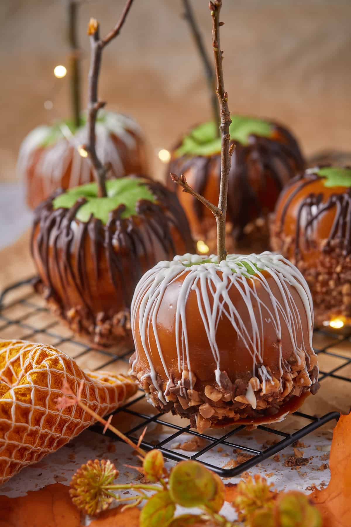 Caramel apples with white and dark chocolate drizzle on black cooling rack.