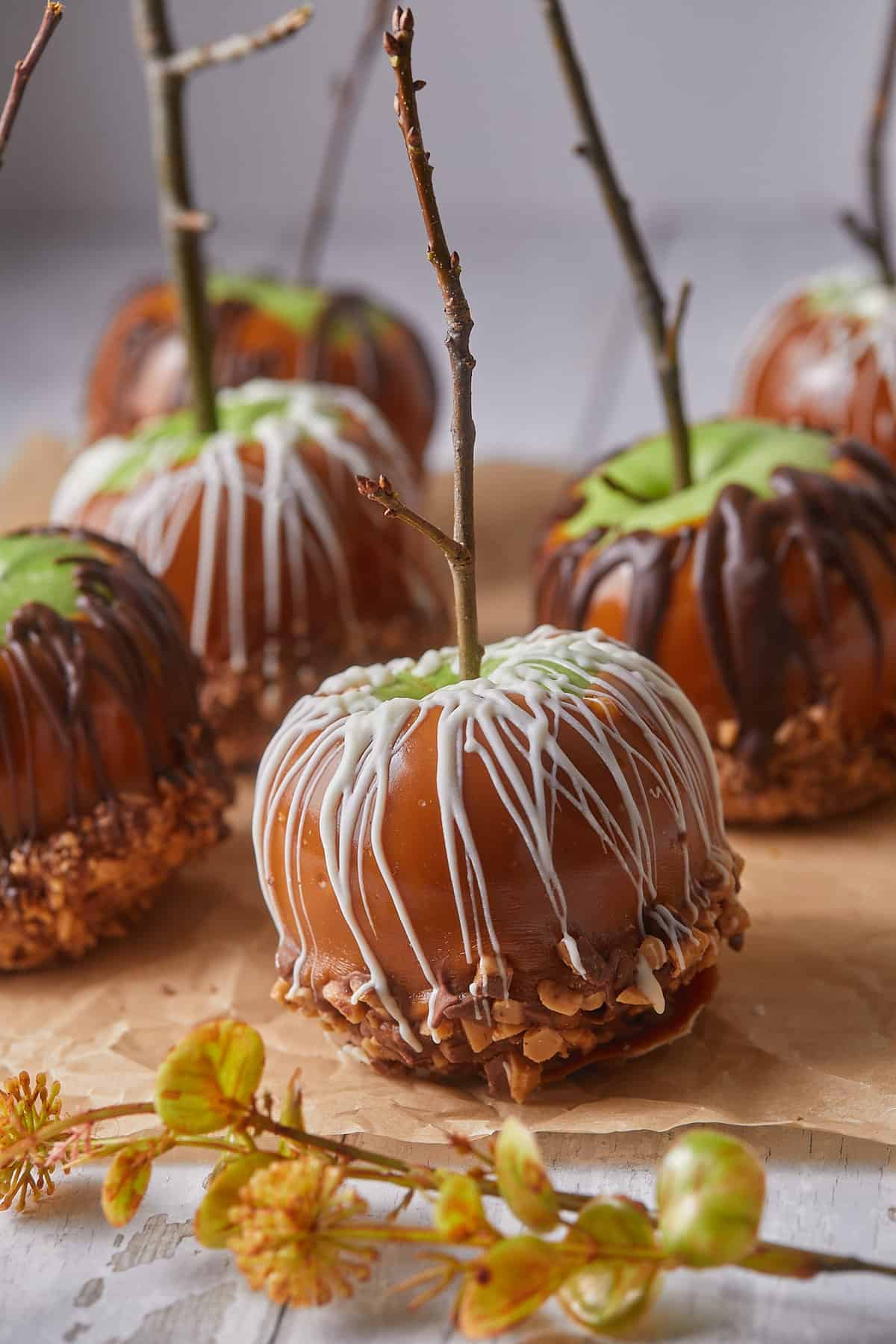 Up close shot of the caramel apples with white chocolate drizzle on parchment. 