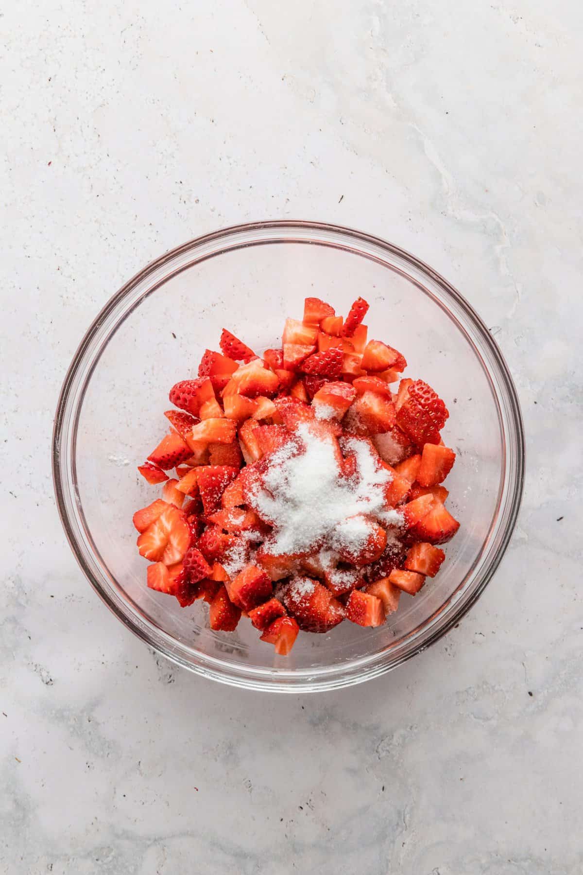 Large glass bowl with diced strawberries and a bit of sugar sprinkled on top.