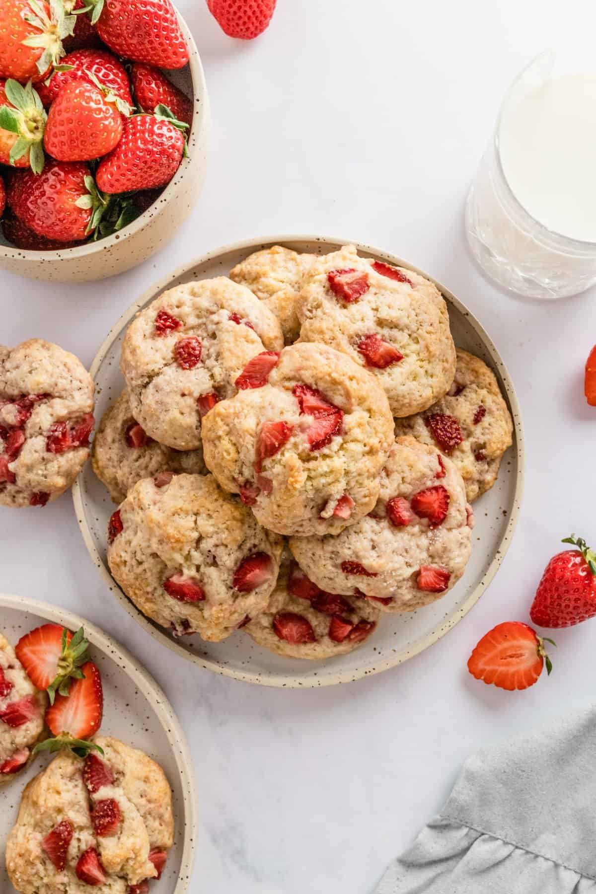 Cookies in center with milk and bowl of strawberries in corners. 