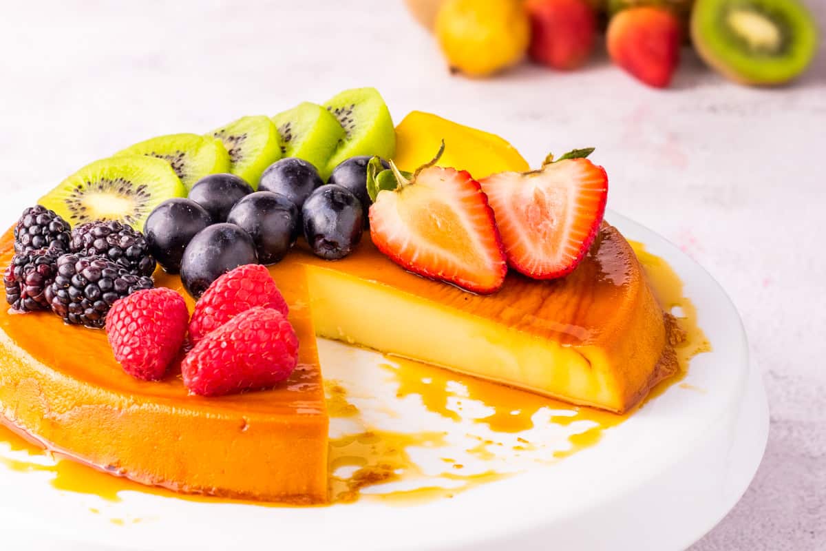 Caramel flan with fruit on top and slice taken out on a white plate. 