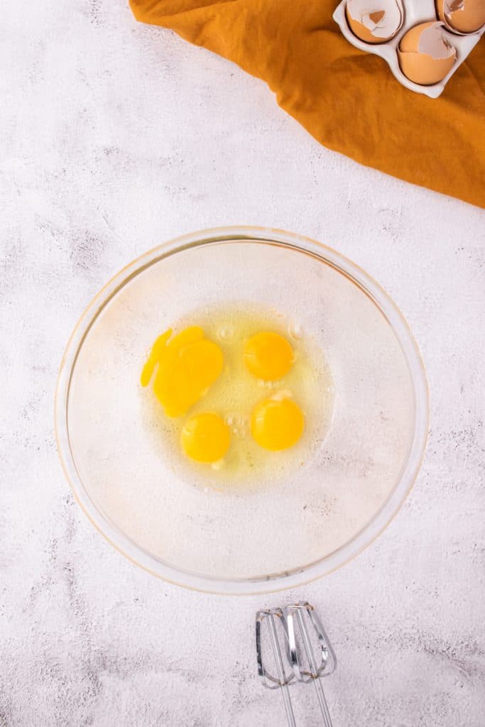 Cracked eggs in a large glass bowl on white surface. 