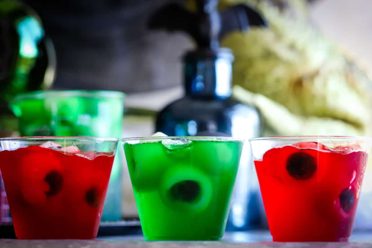 Three small plastic cups with red and green jello and fruit eyeballs. 