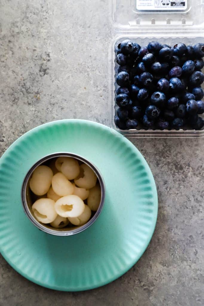 Longan fruit in a can on plate next to a clamshell of blueberries.