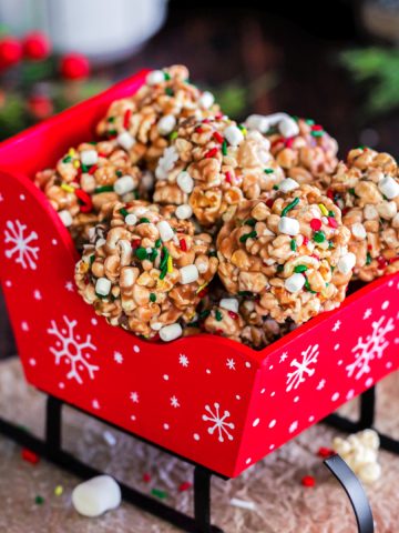 Featured image of the hot cocoa popcorn balls in a small red sleigh.