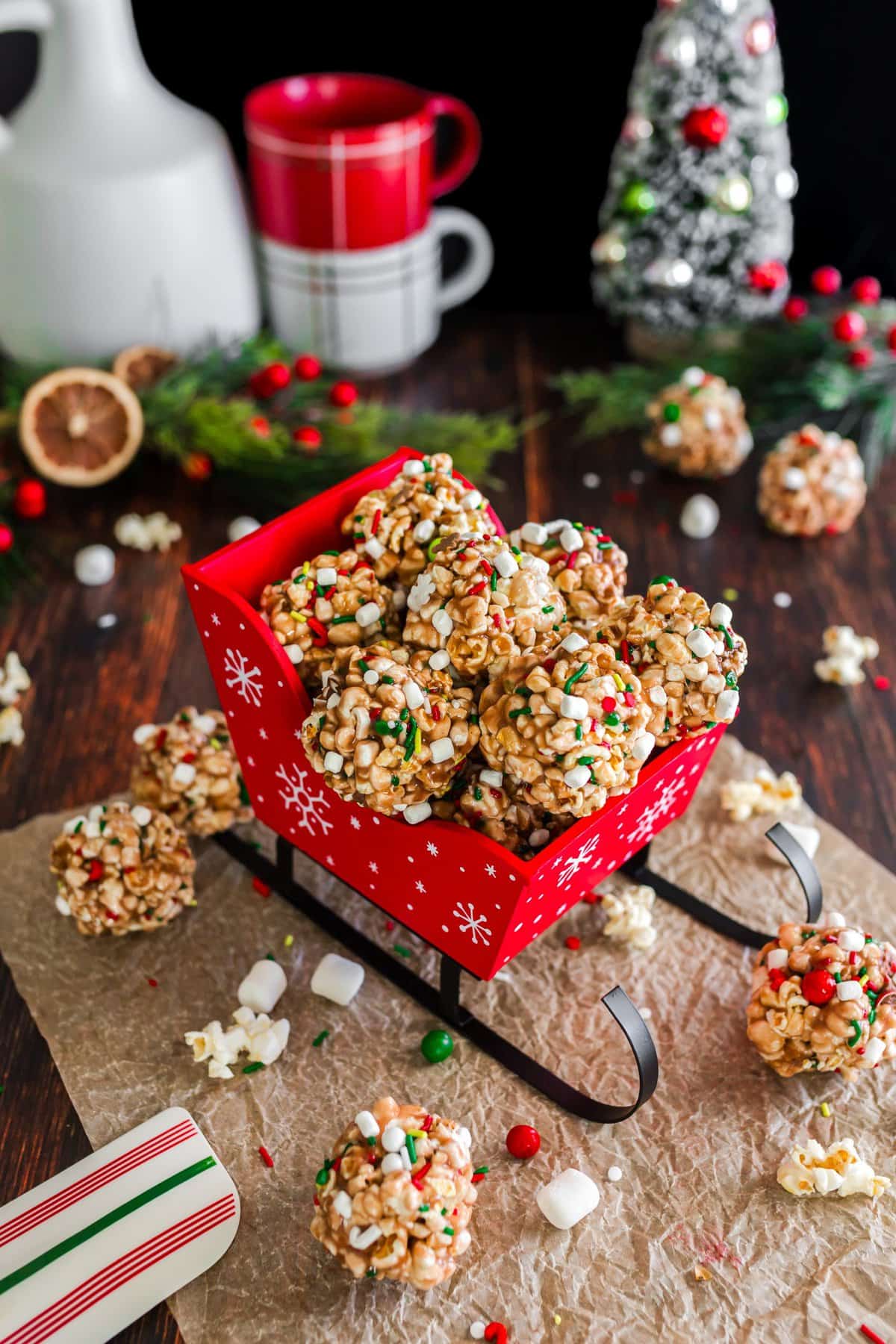 Popcorn balls stacked in a red sleigh with other Christmas decorations in the background. 