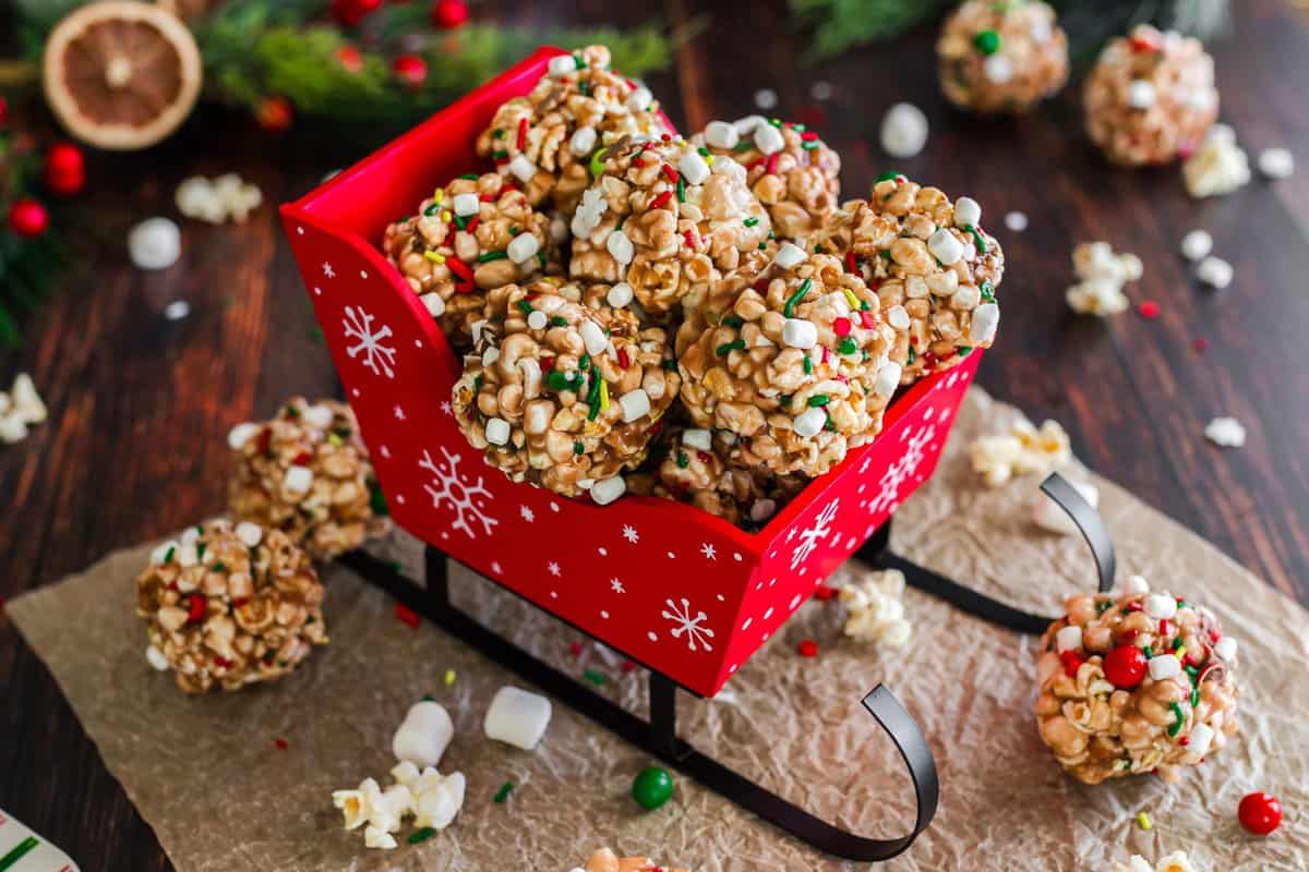Chocolate popcorn balls stacked in a mini red sleigh on a wood background. 