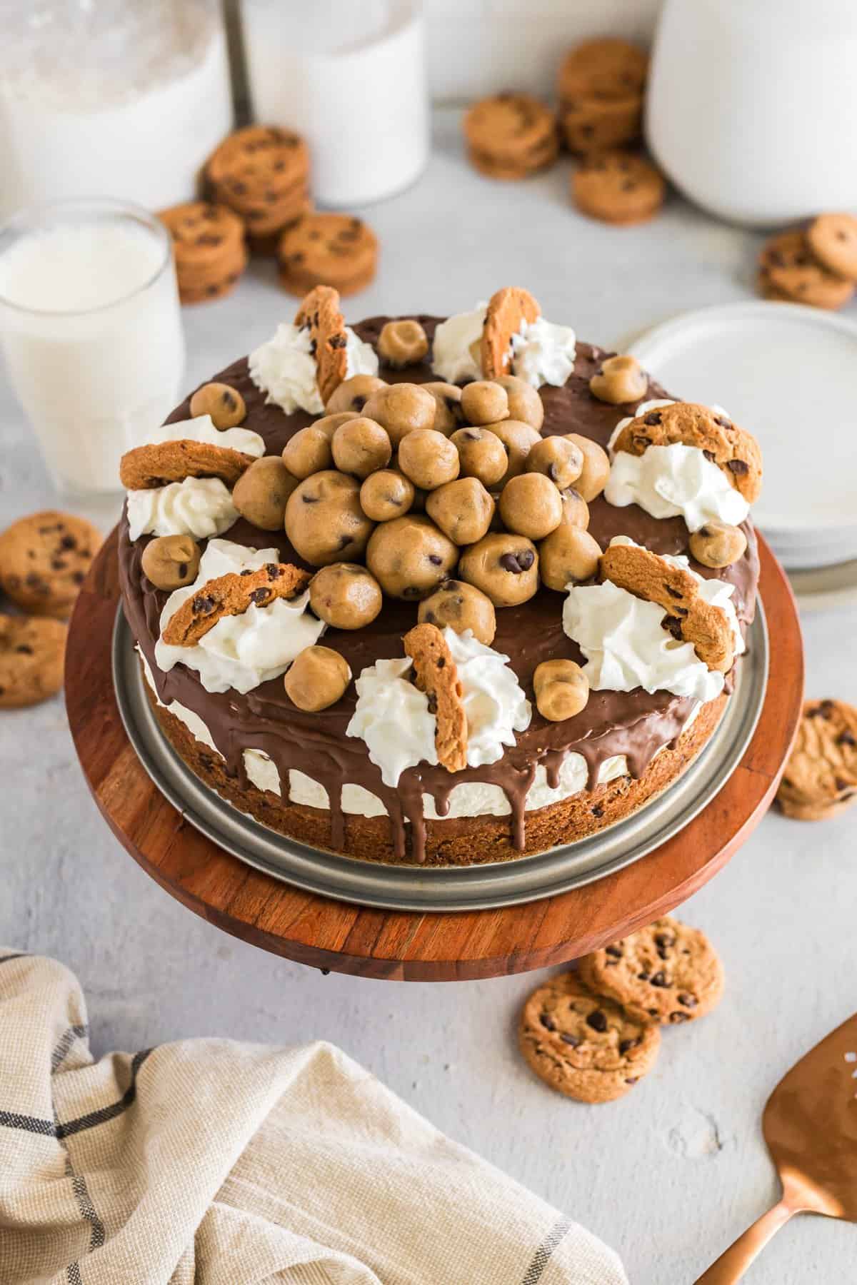 Cheesecake topped with chocolate and cookie dough balls on a wood cake plate. 