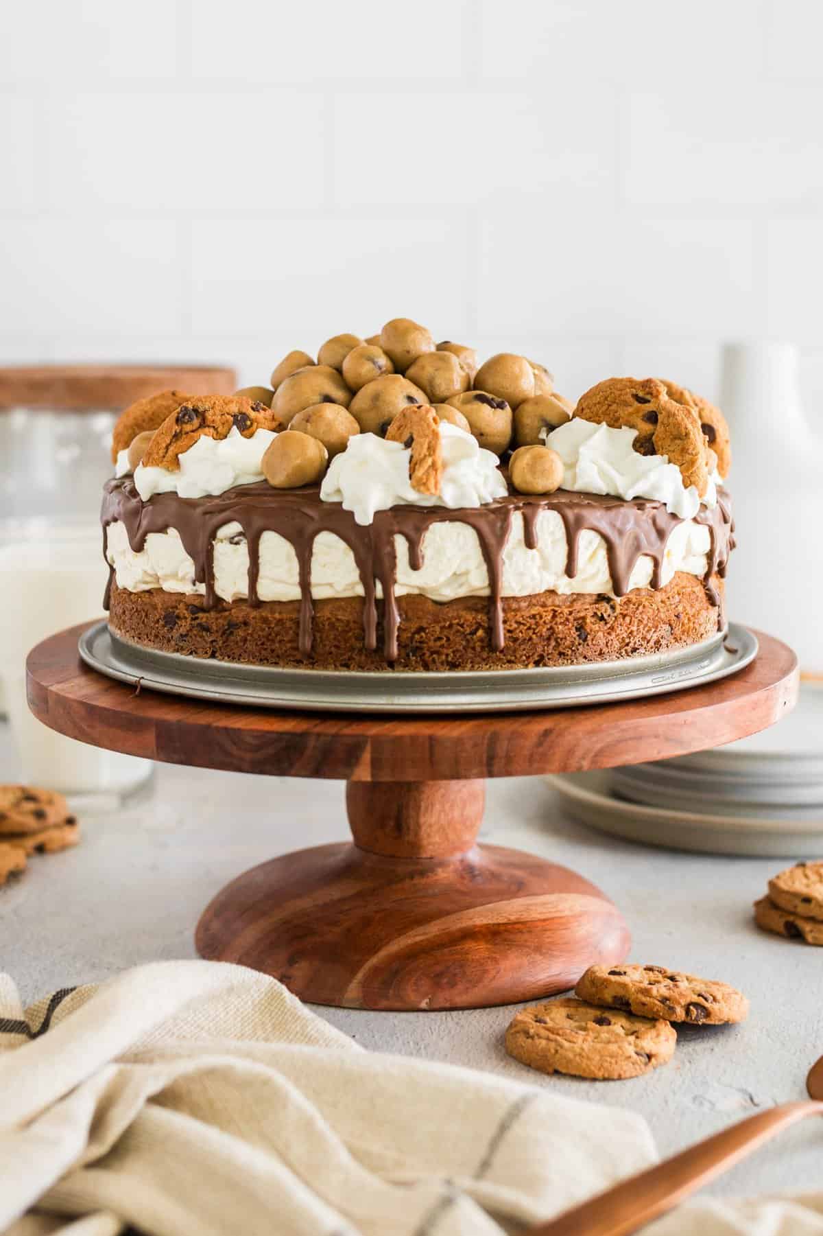 Cookie dough cheesecake on a wooden cake plate with white background. 