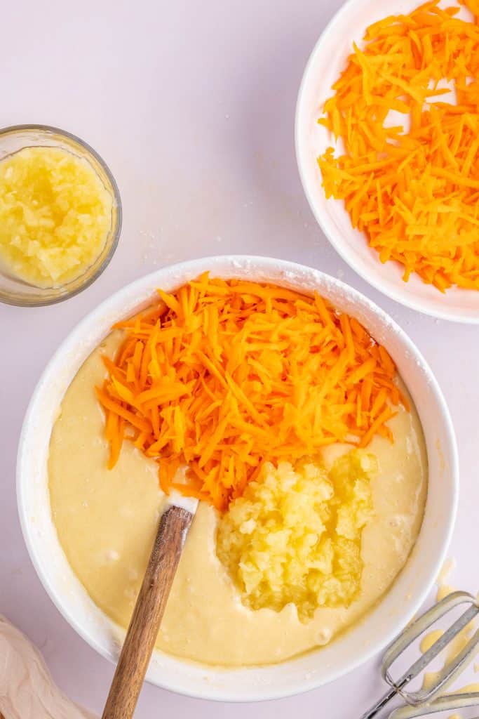 Adding the carrots and pineapple to the cake batter in large white bowl. 