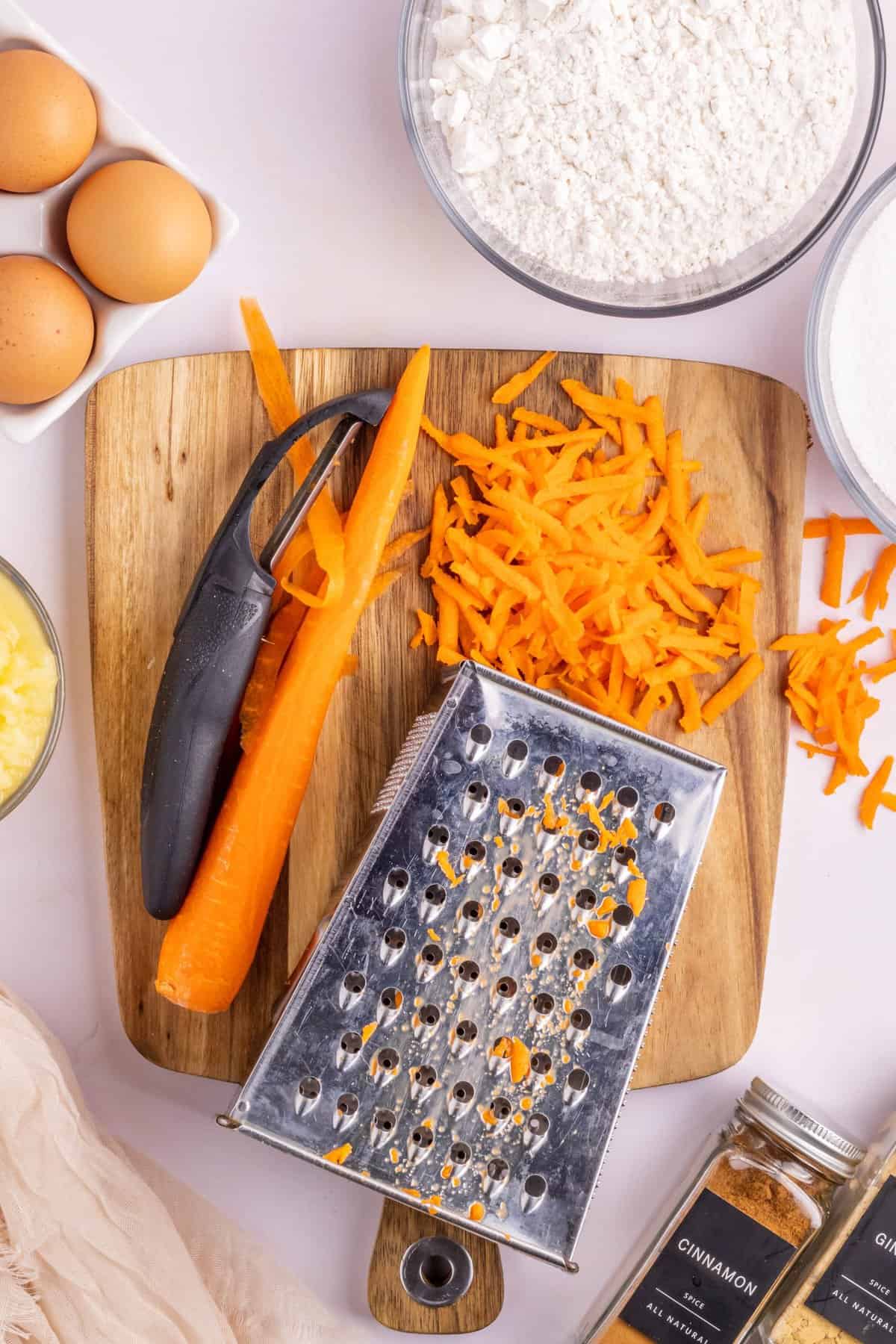 Overhead shot of the grated carrots on a wood cutting board and metal grater. 
