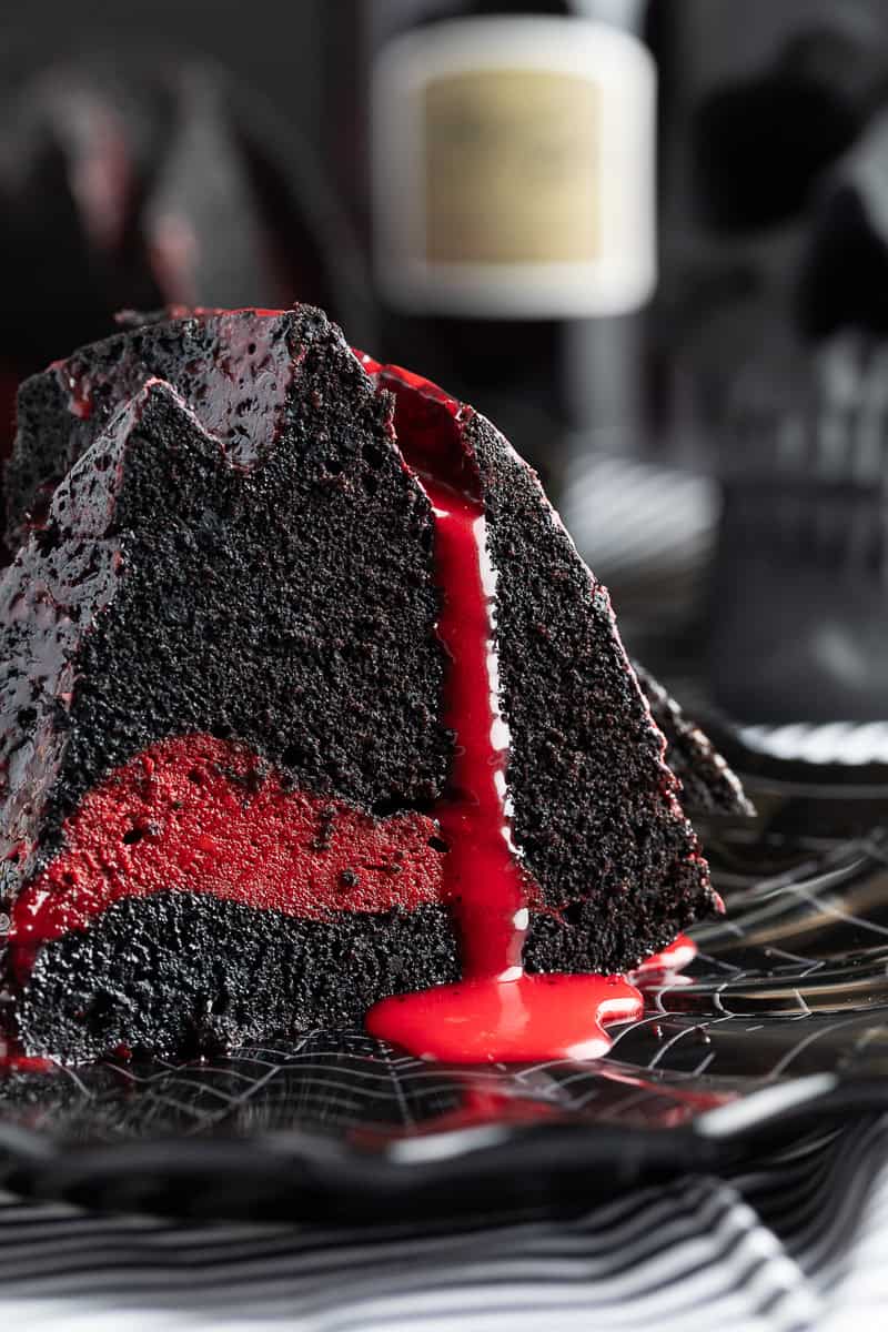 Photo of a slice of bundt cake with red cream cheese center and red ganache flowing over side. 