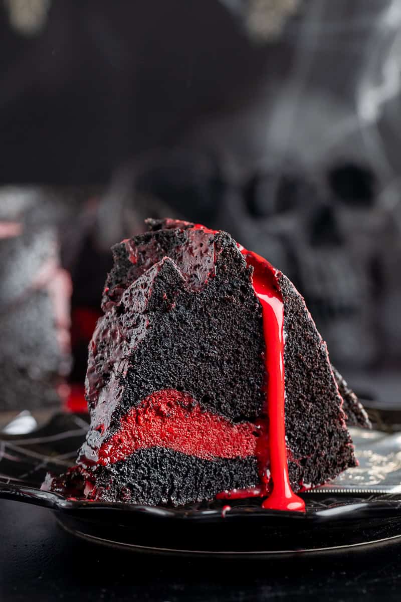 Up close shot of the bundt cake on a black plate with the bloody ganache dripping off the side. 