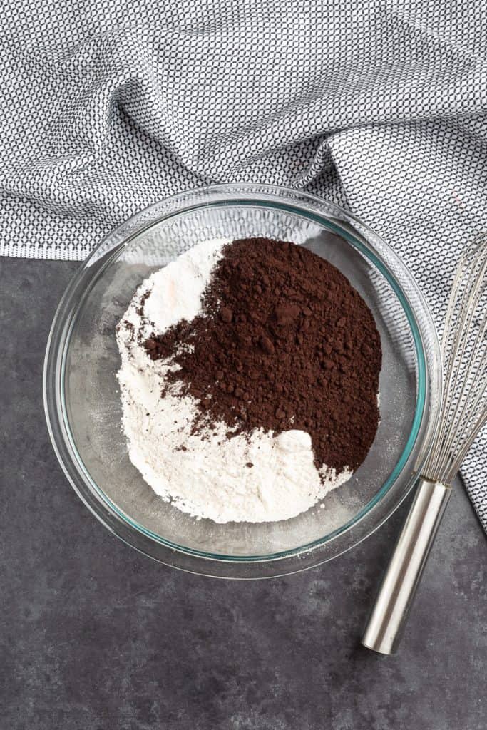 Large glass bowl with flour and dark cocoa powder on black metal background. 