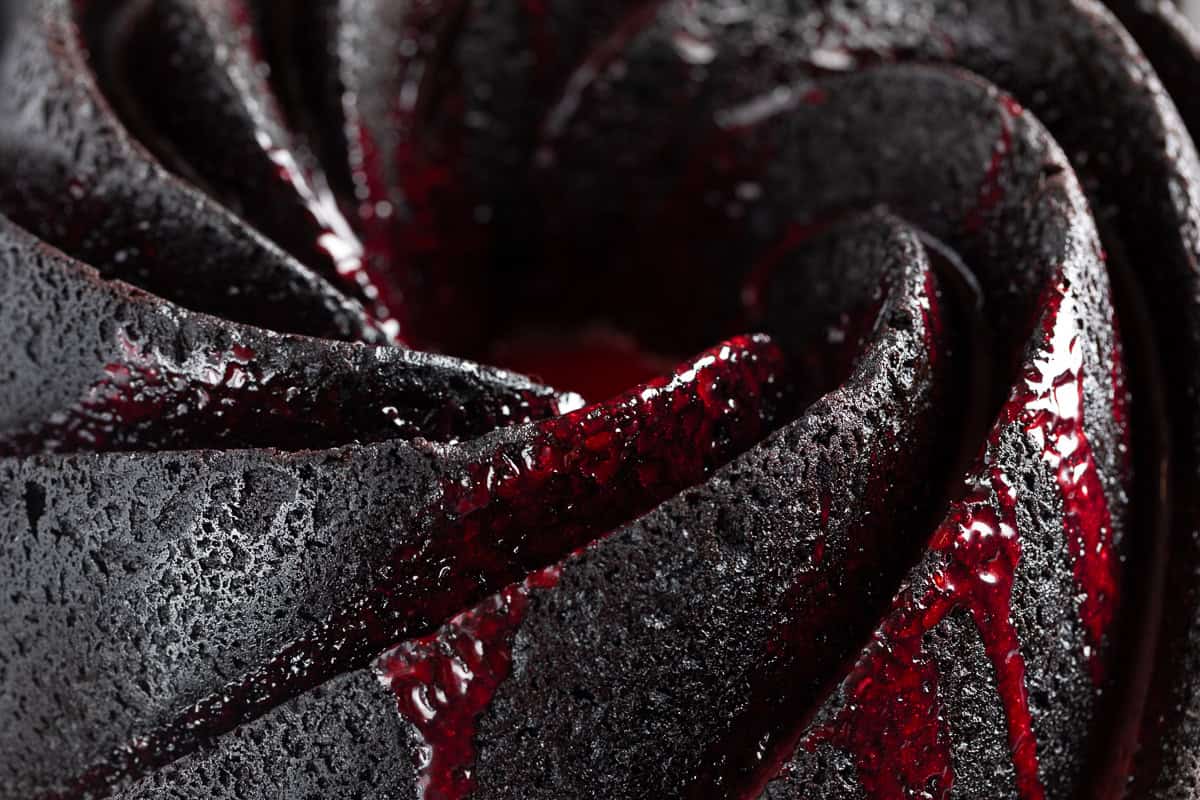 Up close shot of the black bundt cake swirls with red ganache dripping. 