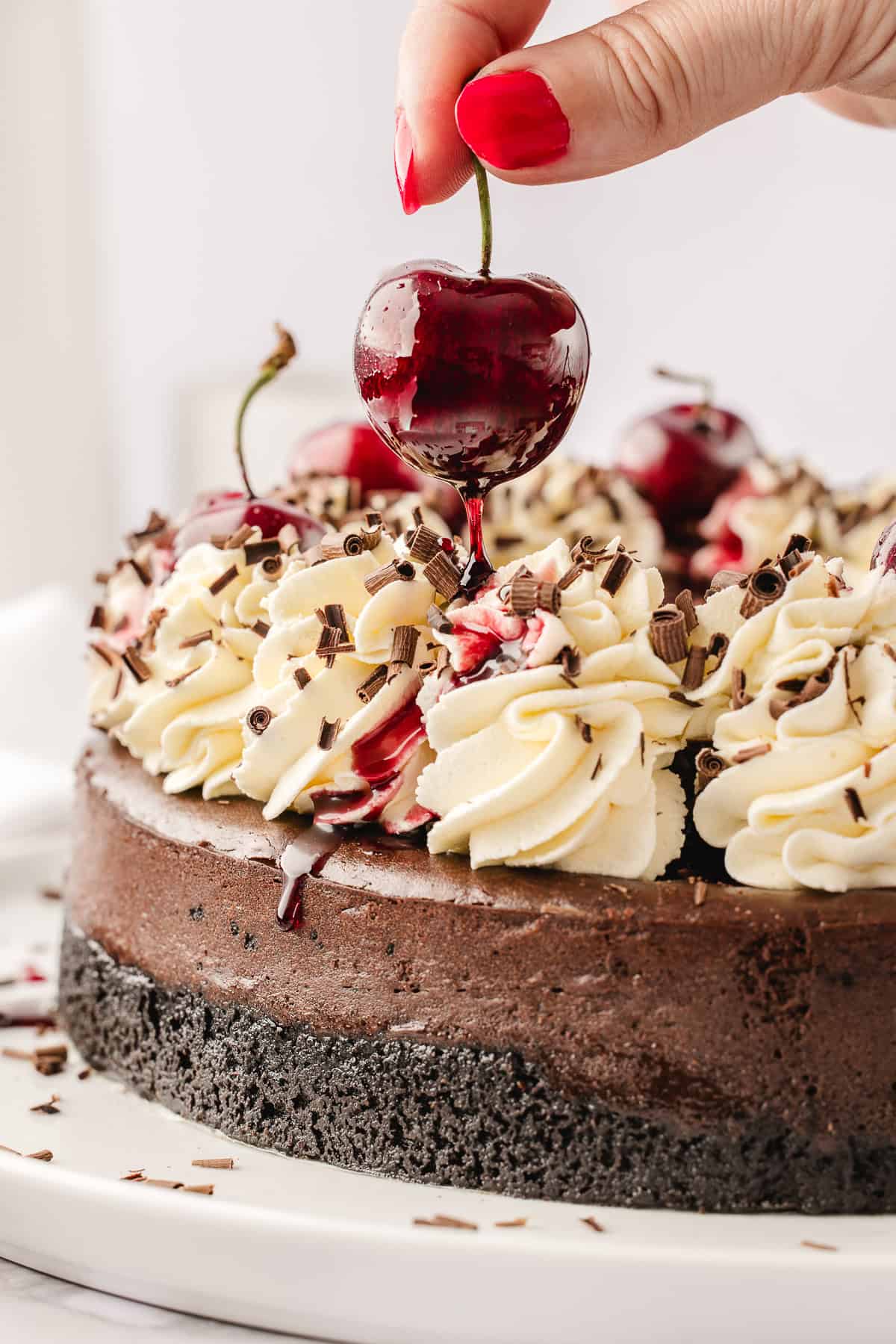 Hand placing a fresh cherry on top of the whipped cream dollops. 