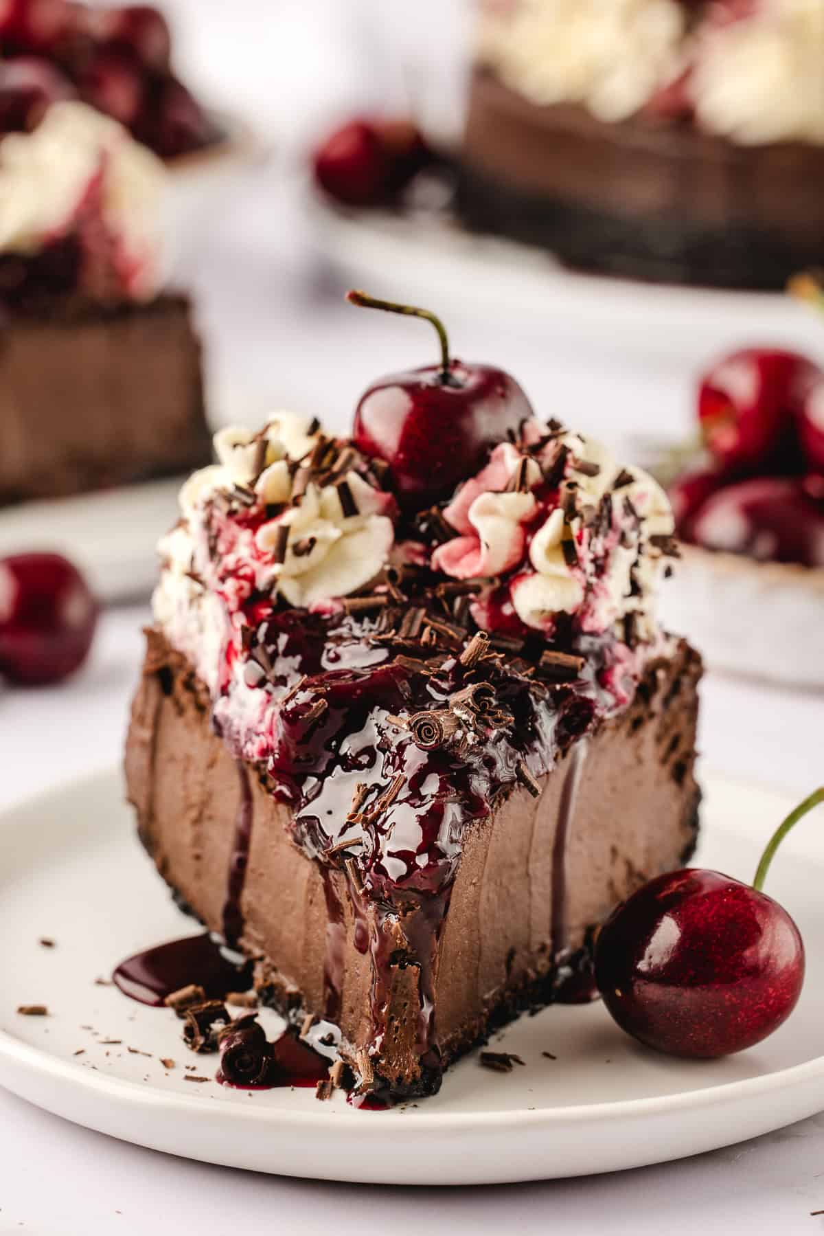 Up close shot of slice of cheesecake on white plate with fresh cherries and chocolate. 