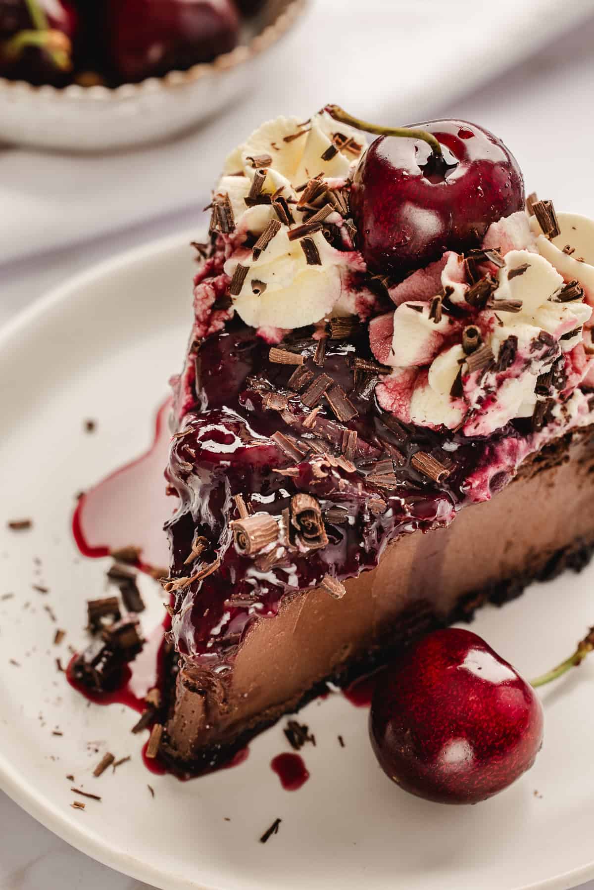 Slice of chocolate cheesecake with chocolate shavings, whipped cream, and fresh cherries. 