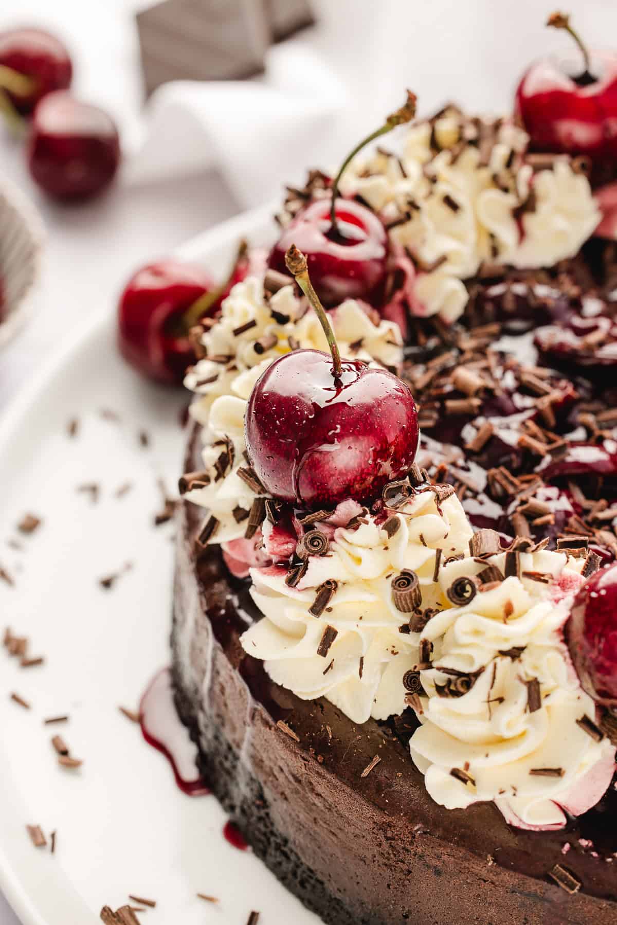 Overhead shot of chocolate cheesecake with whipped cream swirls and cherries. 