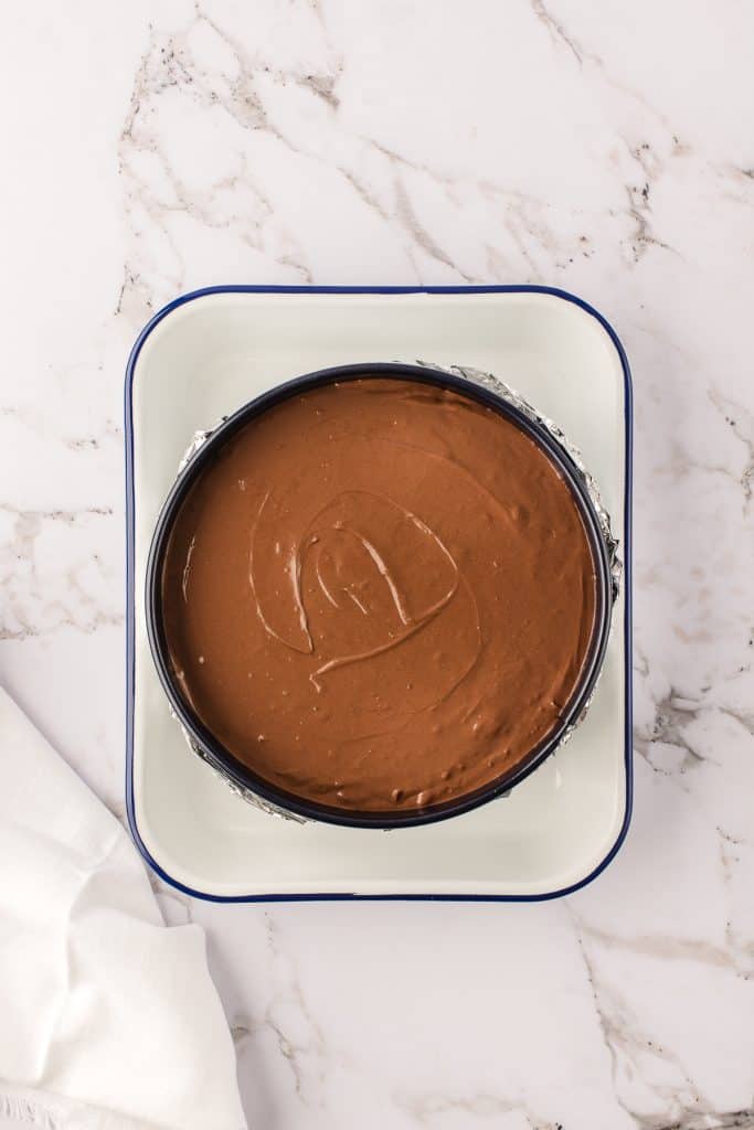 Pouring the chocolate cheesecake batter into the pan and baking.