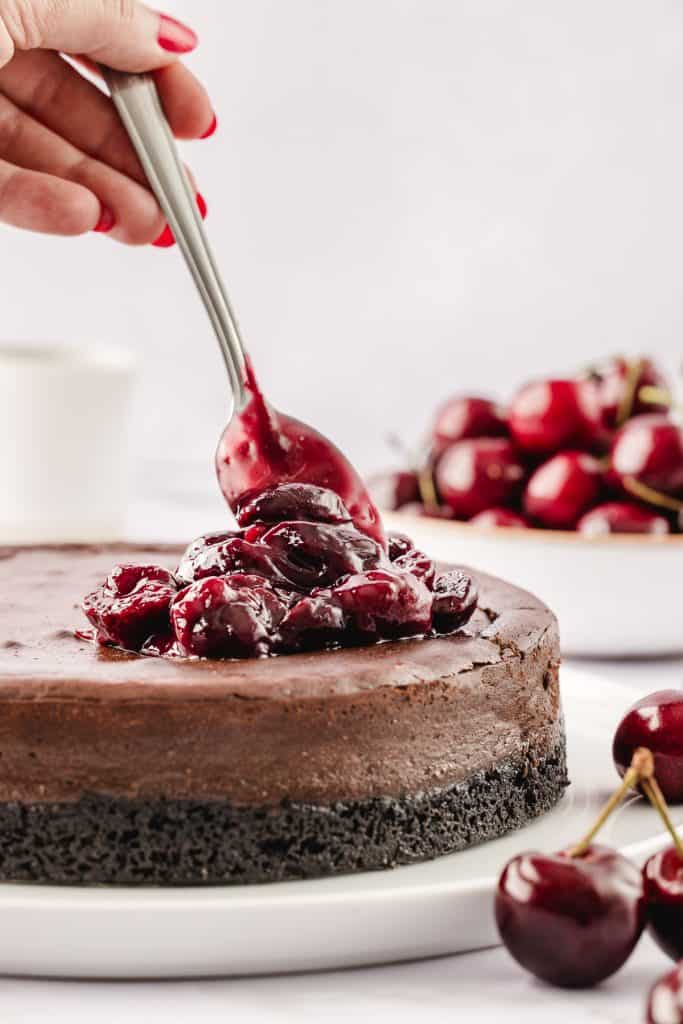 Using a spoon to top the chocolate cheesecake with cherry compote.