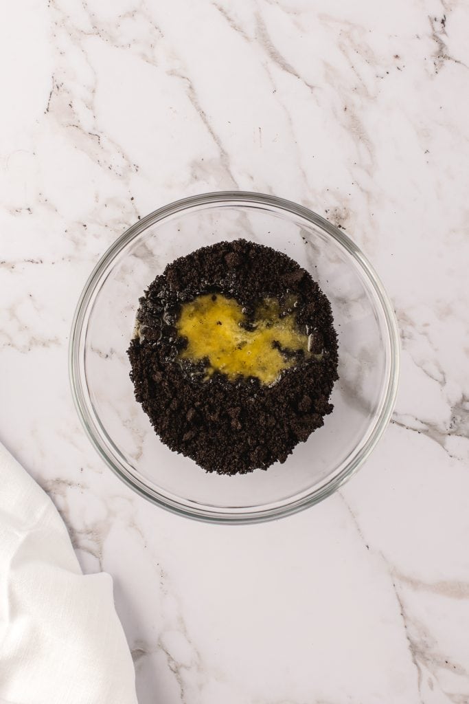 Crushed Oreos and melted butter in a glass bowl on white marble.