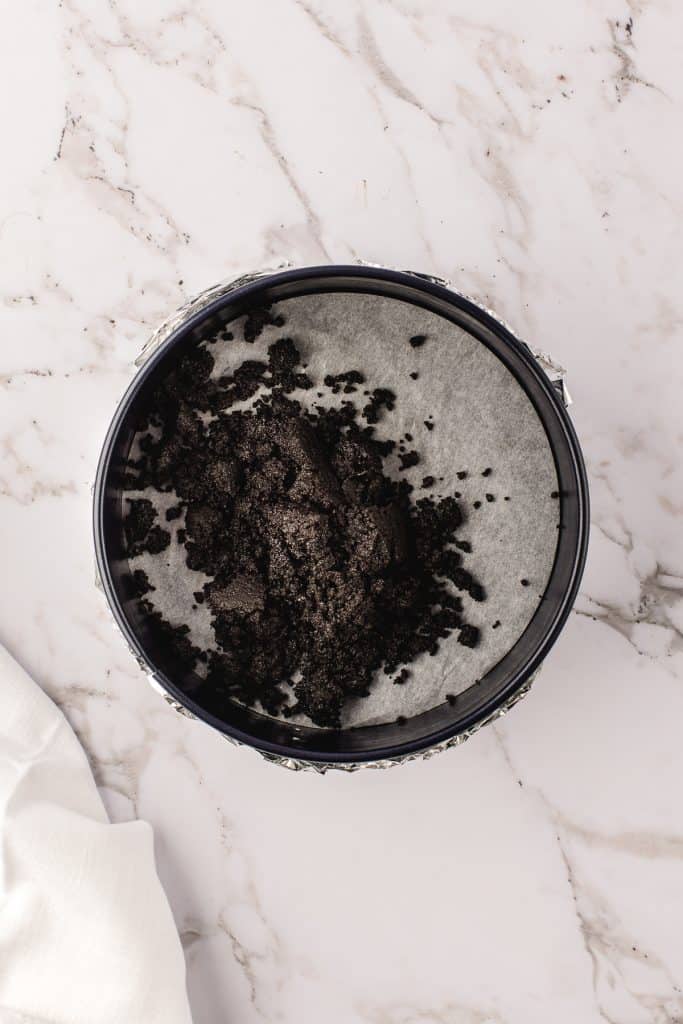 Pouring the Oreo cookie crust into the 9-inch round pan. 