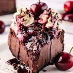 Feature image of slice of chocolate Black Forest cheesecake on white plate.